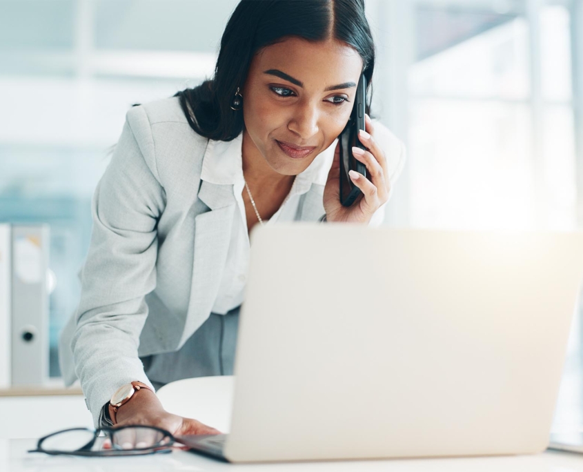 Front view of woman on the phone leaning over laptop while typing