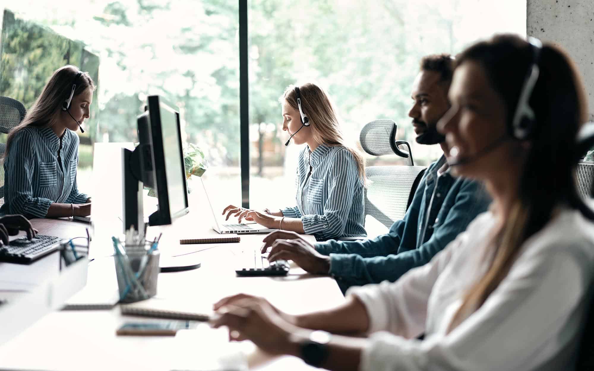 Side view of multiple people with headsets on working on computers