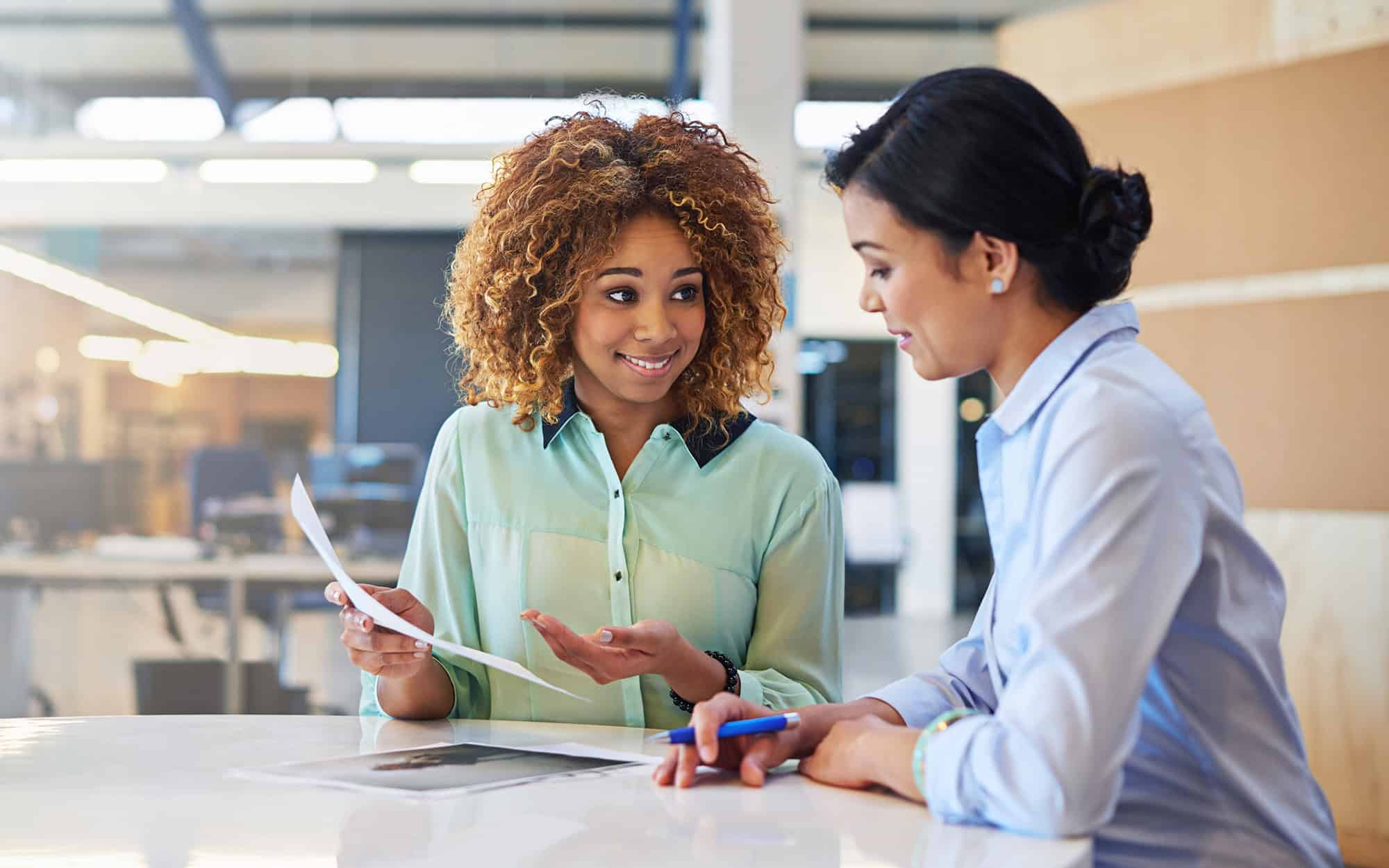 Side view of two young professional women having a meeting and looking at documents