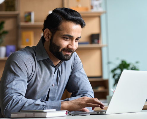 Smiling indian business man working on laptop at home