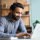 Smiling indian business man working on laptop at home